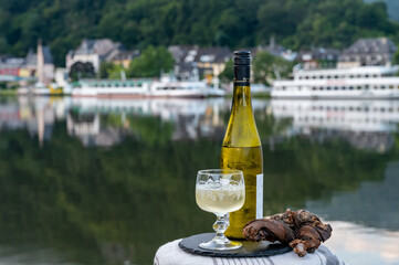 Tasting of white quality riesling wine served on outdoor terrace in Mosel wine region with Mosel river and old German town on background, Germany - obrazy, fototapety, plakaty