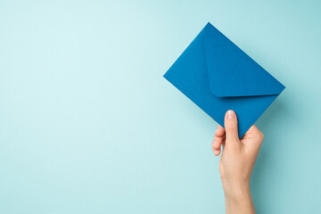 First person top view photo of hand holding closed blue envelope on isolated pastel blue background with copyspace - obrazy, fototapety, plakaty