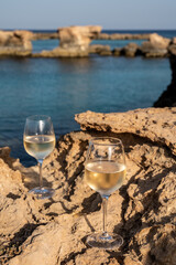 Two glasses of cold white dry white wine served on rocks in blue sea bay near Protaras touristic town on Cyprus