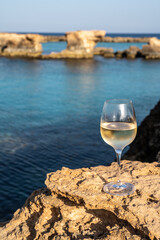 Glass of cold white dry white wine served on rocks in blue sea bay near Protaras touristic town on Cyprus
