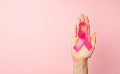 First person top view photo of female hand holding pink ribbon in palm symbol of breast cancer...