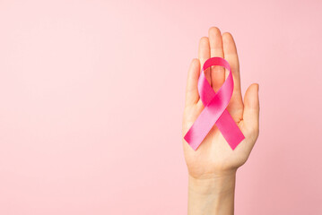 First person top view photo of hand holding pink ribbon in palm symbol of breast cancer awareness...