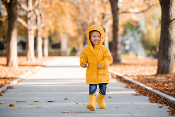Pretty funny kid girl 2-3 year old wear yellow bright raincoat, rubber boots walk in park over...