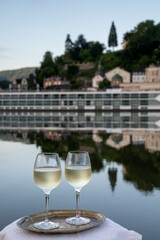 Tasting of white quality riesling wine served on outdoor terrace in Mosel wine region with Mosel river and old German town on background, Germany