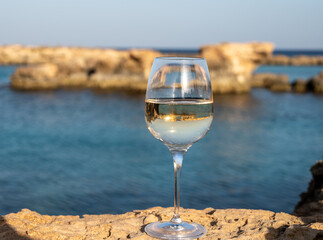Glass of cold white dry white wine served on rocks in blue sea bay near Protaras touristic town on...