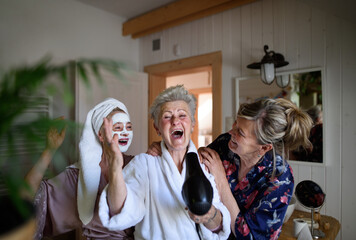 Happy senior women friends in bathrobes having fun indoors at home, selfcare concept.