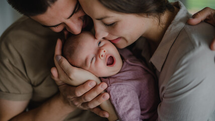 Close up of young parents holding and kissing their newborn baby indoors at home - obrazy, fototapety, plakaty