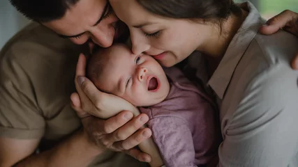 Fototapeten Close up of young parents holding and kissing their newborn baby indoors at home © Halfpoint