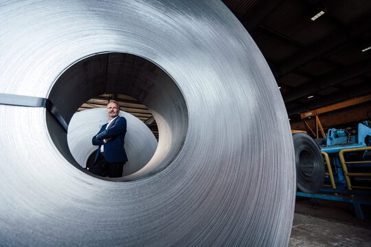 Senior businessman with arms crossed standing at by rolled up metal sheet