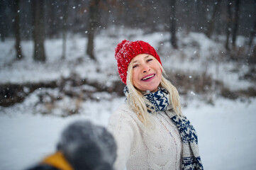 Front view portrait of happy senior woman with hat outdoors standing in snowy nature, looking at camera.