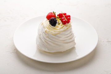 dessert Anna Pavlova with berries on white plate on white concrete table