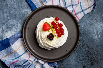 dessert Anna Pavlova on dark blue table with strawberry, red currant and blueberry top view