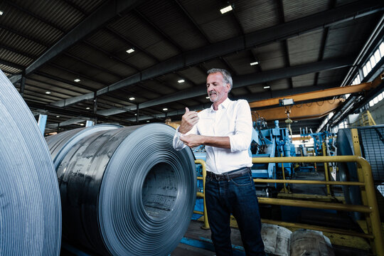 Senior businessman rolling sleeves while standing in steel mill