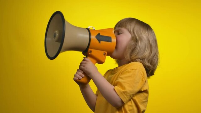 Girl in a yellow t-shirt is creaming in a megaphone on yellow background studio