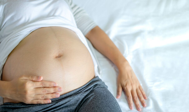 Image of A woman pregnant reclining on bed and touching or caressing her belly with hands. Motherhood, pregnancy, gynecology and health care concept.