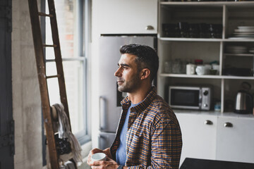 Hispanic mid adult male having morning coffee and looking out of the window