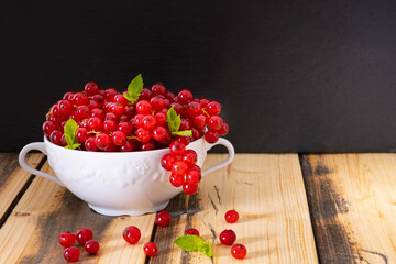 ripe fragrant currants in a white bowl, some berries fell out, on a wooden table