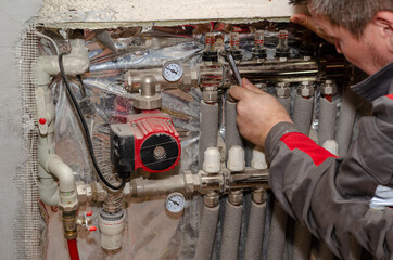 Repair and service concept heating systems. Specialist inspects floor heating system. Adult male checks the tightness of the pipes on the water manifold. Selective Focus. Indoors. Series part.