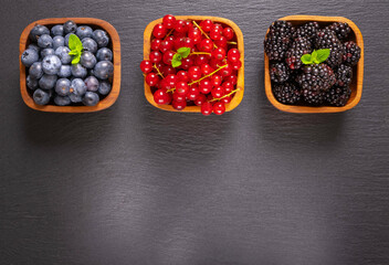 full wooden bowls of ripe berries - blueberries, currants and blackberries and mint leaves