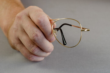 One hand holds an empty metal eyeglass frame against a gray background. A man shows the Yellow frame. Close-up. Selective focus.