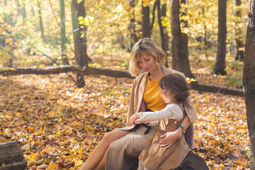 Beautiful lifestyle autumn photo mother and child walks evening in the park, warm sunlight.