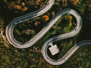 Aerial view of winding curved road with helipad and colourful autumn foliage in Italy