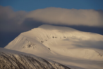 Storm clouds rolling up behind a snowy peak in Norway