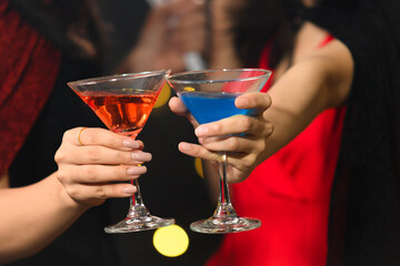 close-up colorful cocktail glasses of two young woman in witch halloween costumes in halloween party over dark magic background - Holiday party concept.