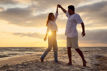 Happy couple dancing on beach at sunset