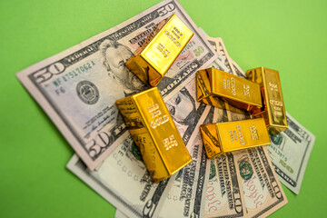 on a bright green background lie dollar bills with gold bars on top of them