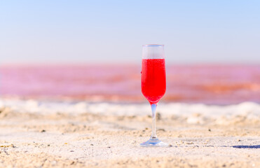 A glass with a pink drink on the white shore of a pink lake. Fabulous and romantic atmosphere. Selective focus on the glass.
