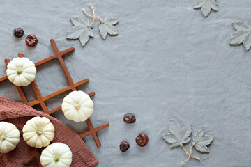 Autumn background with natural pumpkins, chestnuts and decorative grey concrete maple leaves. Flat lay, top view on dark wood and grey linen textile. Natural Fall background in brown and grey.