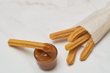 Traditional churros with sugar and cinnamon served on a marble table, with a bowl of caramel.