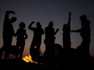 Group of friends having party near bonfire in evening. Camping season