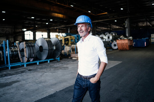 Cheerful male engineer with hand in pocket walking in steel mill
