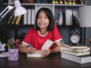 Happy smiling school girl pupil studying at home sitting at desk. Smart cute kid primary school...