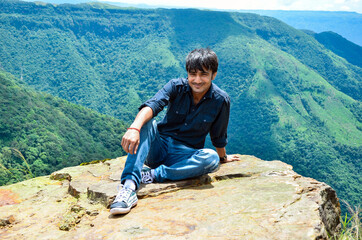 Naklejka na ściany i meble Long shot of a young man sitting at the edge of a mountain cliff, 4500 feet above from the ground