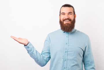 Confident bearded man wearing shirt is presenting you something over white background.