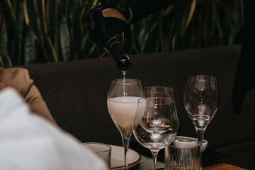 Elegant waiter pours champagne from bottle into glass at restaurant. Sommelier tasting white sparkling wine in restaurant. Copy space for text menu elegant or recipe on dark background.