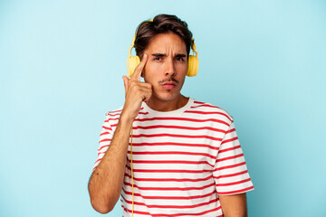 Young mixed race man listening to music isolated on blue background pointing temple with finger, thinking, focused on a task.
