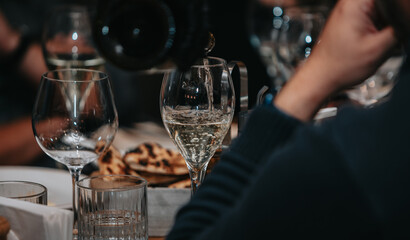 Elegant waiter pours champagne from bottle into glass at restaurant. Sommelier tasting white sparkling wine in restaurant. Copy space for text menu elegant or recipe on dark background.