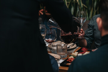 Fototapeta na wymiar Elegant waiter pours red wine from bottle into glass at restaurant. Sommelier tasting wine in restaurant. Copy space for text menu elegant or recipe on dark background.