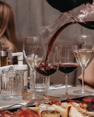 Elegant waiter pours red wine from bottle into glass at restaurant. Sommelier tasting wine in restaurant. Copy space for text menu elegant or recipe on dark background.