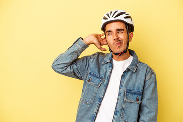 Young mixed race man wearing a helmet bike isolated on yellow background touching back of head, thinking and making a choice.