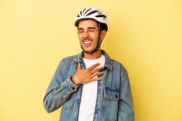 Young mixed race man wearing a helmet bike isolated on yellow background laughs out loudly keeping hand on chest.