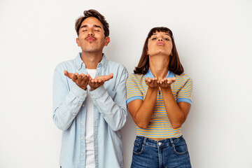 Young mixed race couple isolated on white background folding lips and holding palms to send air kiss.