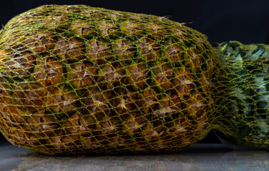 whole pineapple in a mesh with a pronounced texture, lying on a wooden table, on a black background