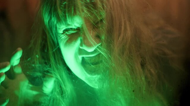 Scary ghost woman screaming through dirty glass on dark background. Monster devil or female spirit dead characters.