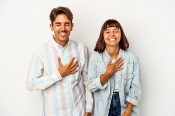 Young mixed race couple isolated on white background laughs out loudly keeping hand on chest.