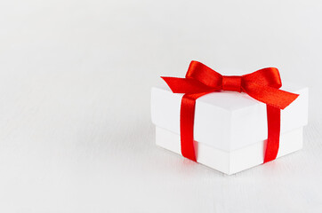 White present box with red satin ribbon and bow on white table, top view, copy space. Festive background for design of card, brochure, cover, flyer.
